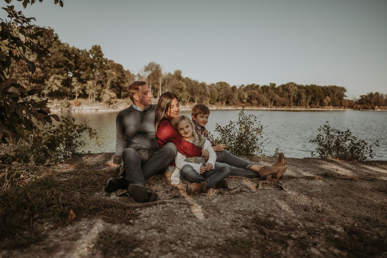 A family relaxes together on rocks by a serene lake during an autumn afternoon.