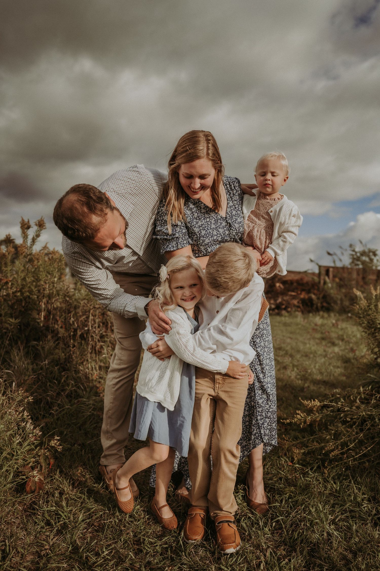 Intimate family embrace captured during outdoor photo session with moody sky backdrop.