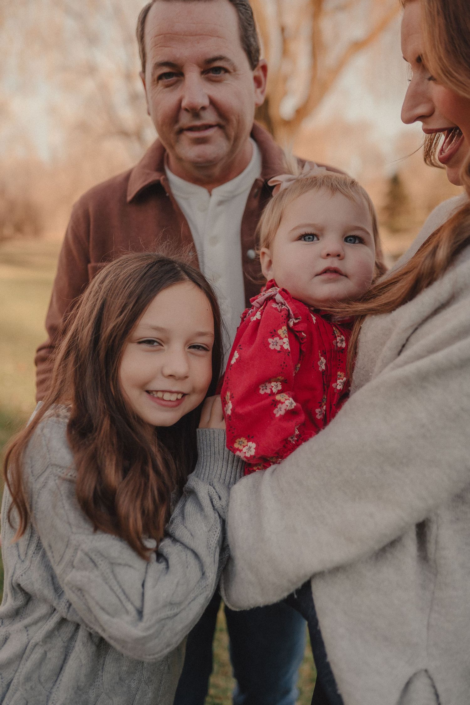 Family wearing coordinated neutral outfits embraces during an outdoor autumn photoshoot.