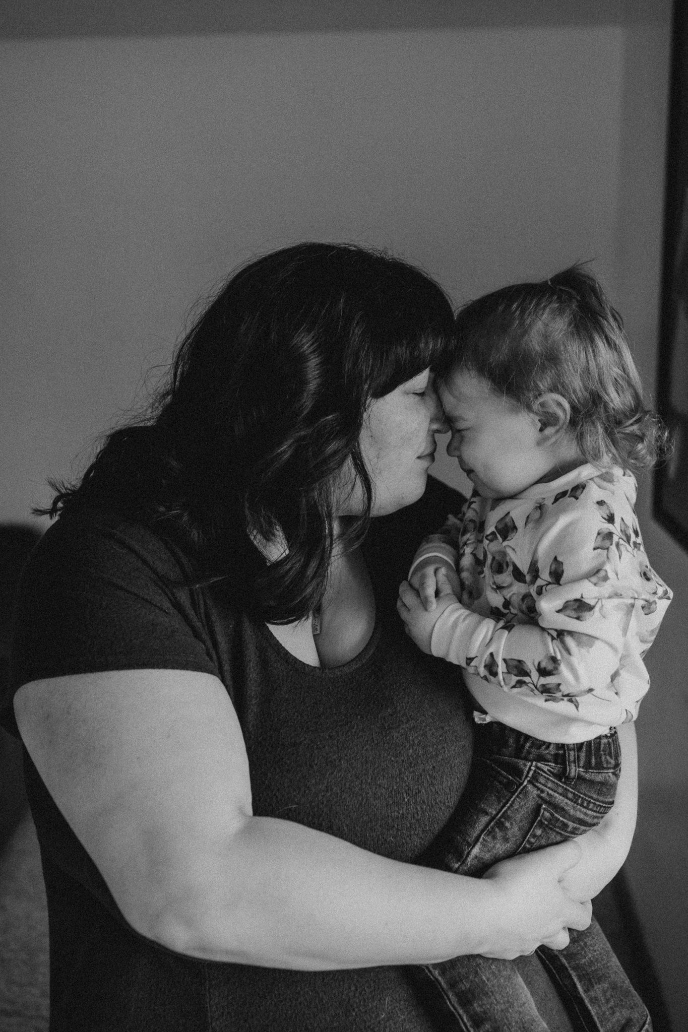 Intimate black and white portrait showing tender moment with toddler in floral outfit.