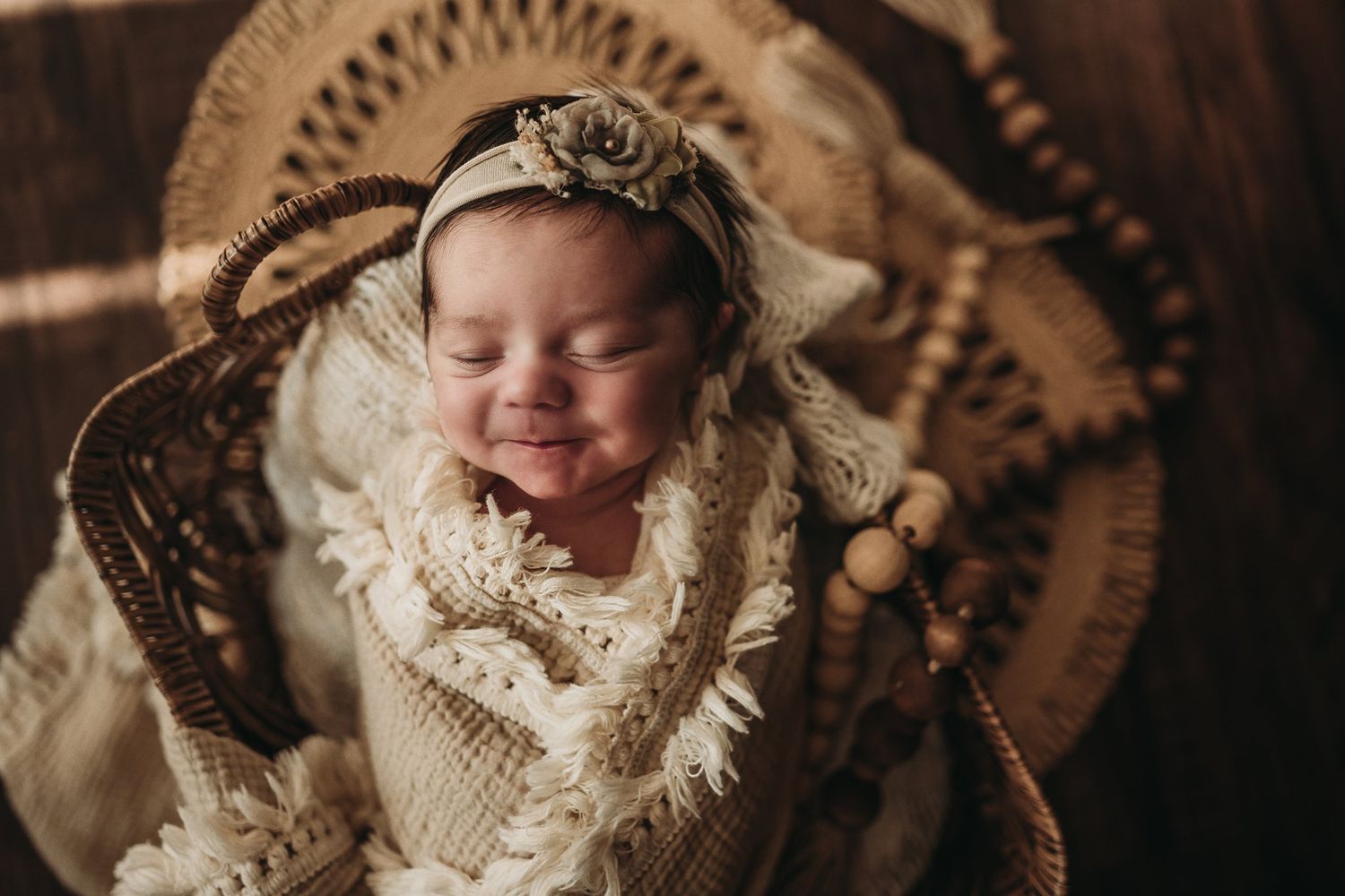Smiling baby wrapped in cream knit blanket with decorative headband in wicker basket.