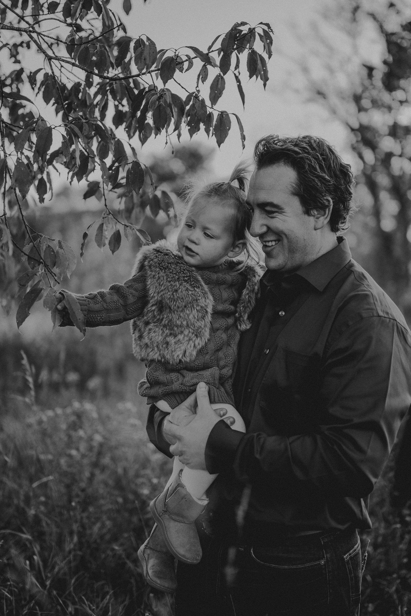 Black and white candid moment showing parent and child exploring leaves.