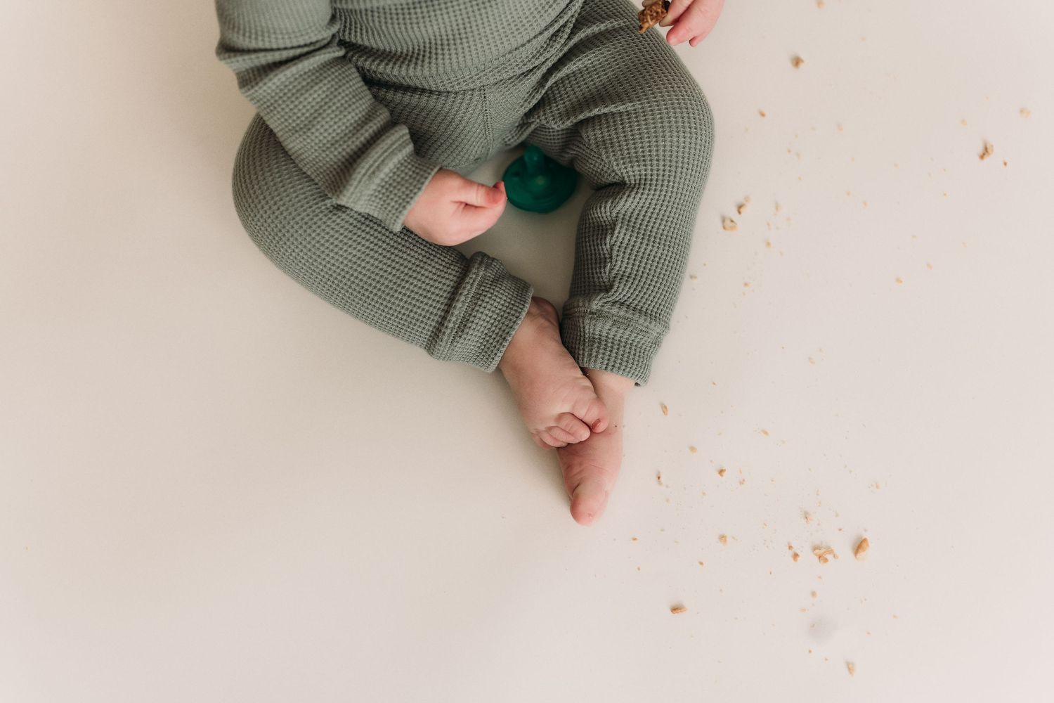 Close-up shot of small feet in a sage green knit outfit against a white background.