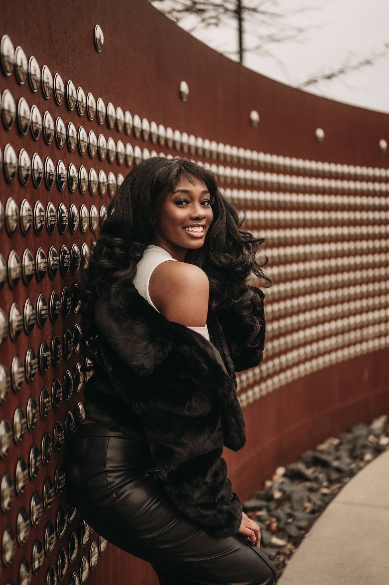Model smiles while posing against geometric patterned wall in winter fashion ensemble.