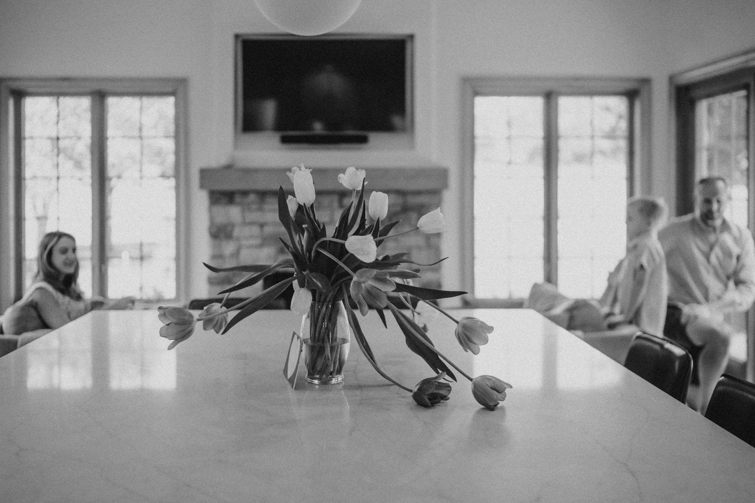 Black and white photo of modern living room with floral centerpiece on dining table.