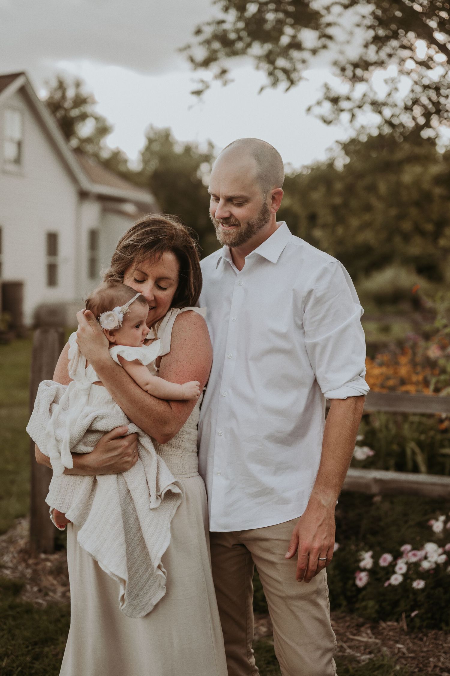 Intimate family moment captured in warm tones near flowering garden and white farmhouse.