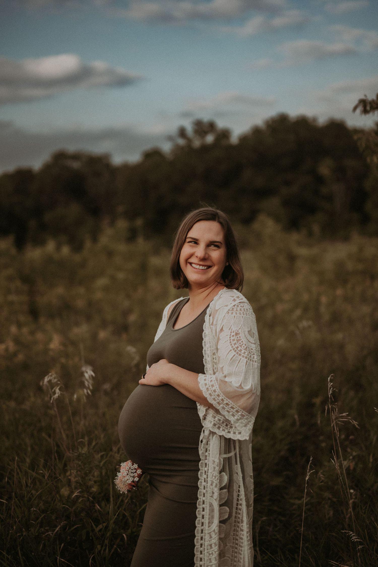 A joyful maternity portrait featuring a woman in a lace cardigan at sunset.