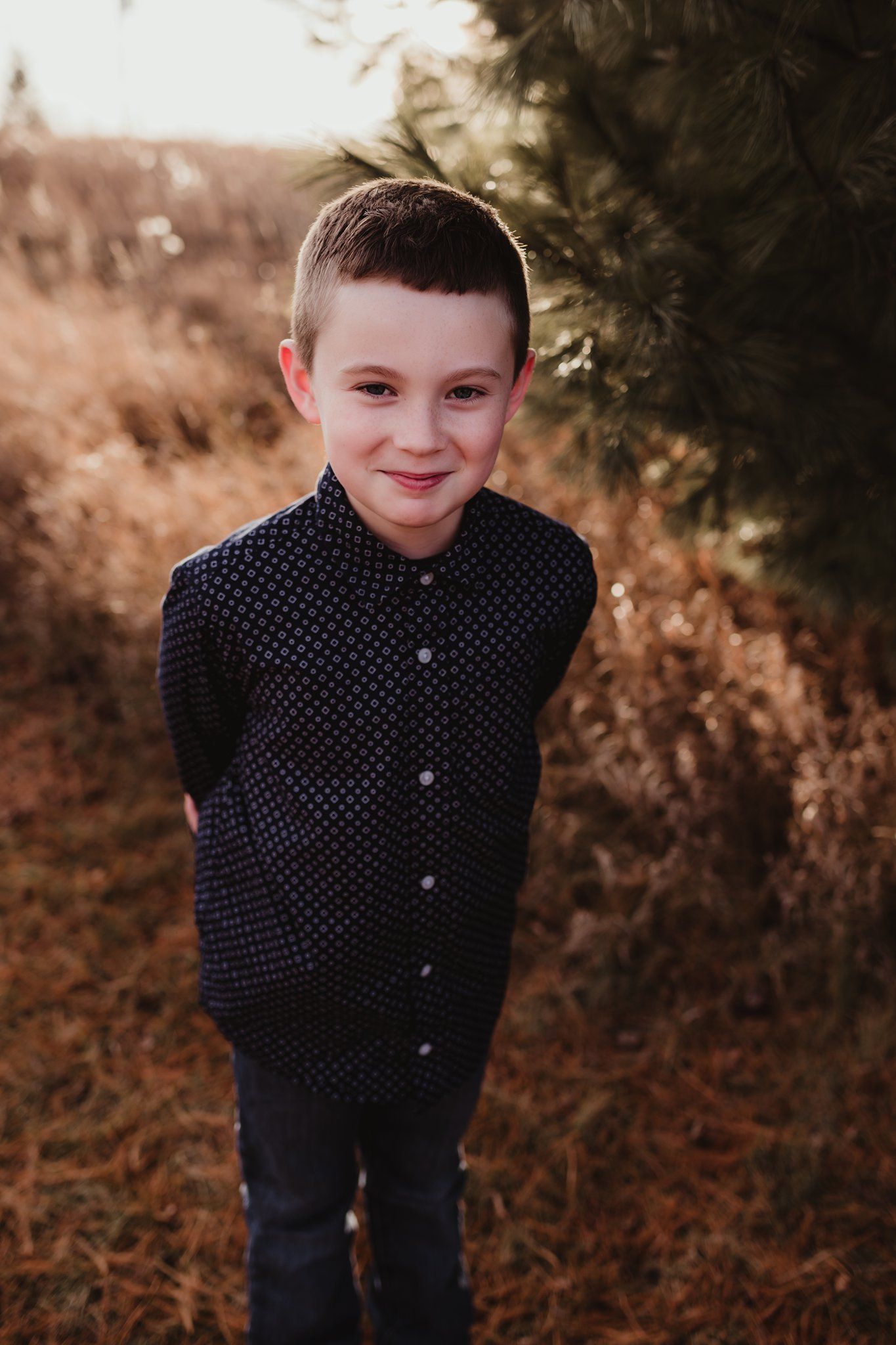 Portrait of a smiling child in a navy polka dot shirt against an autumn background.