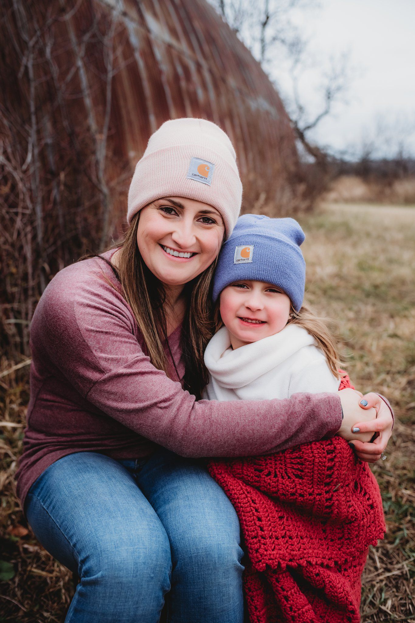 A cozy winter outdoor portrait against rustic barn wall wearing knit beanies and warm clothing.