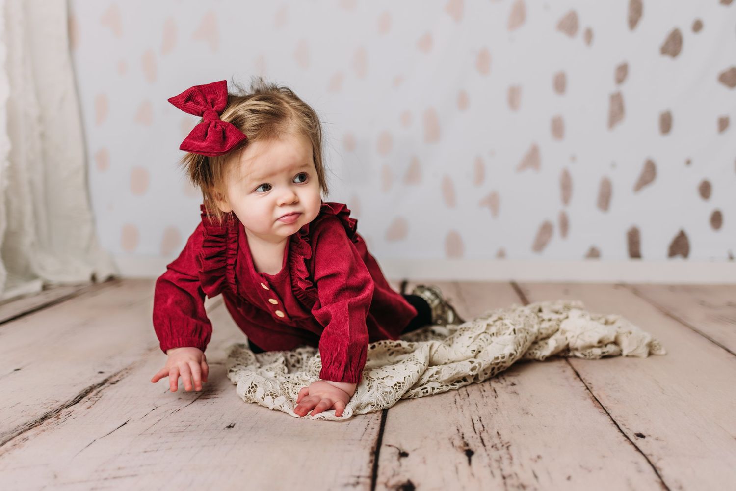 Baby in red outfit crawling on rustic wooden floor with patterned wall.