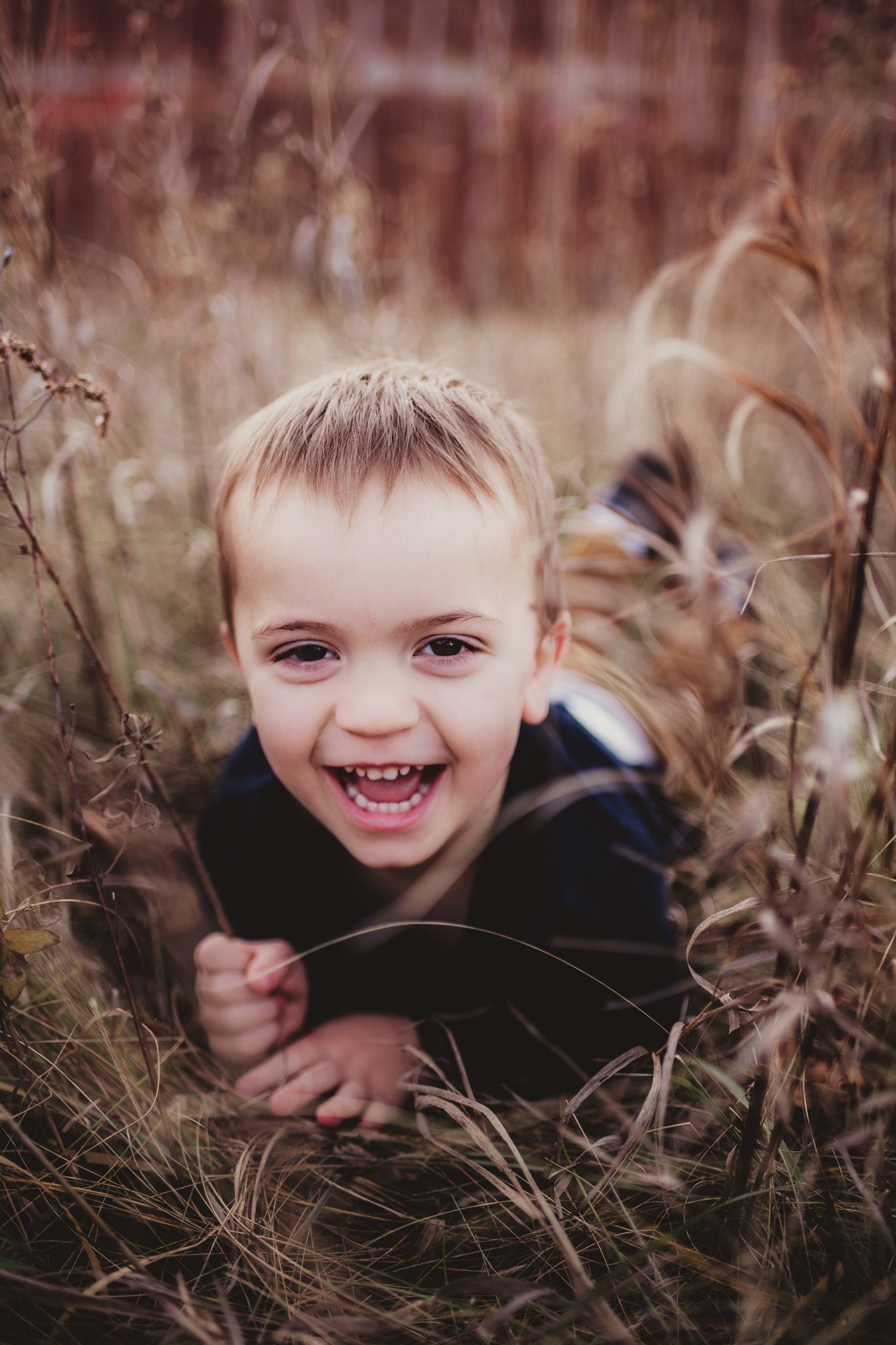 A joyful expression captured among tall grass during an outdoor photo session.