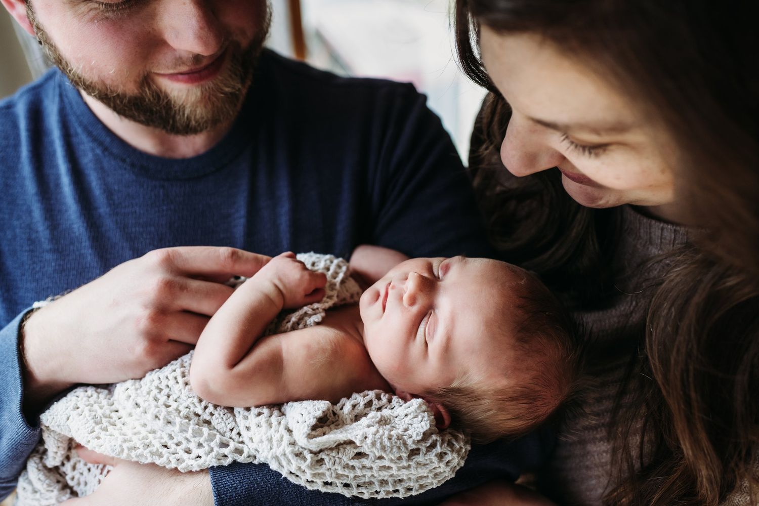 An intimate family moment as parents gaze lovingly at their newborn baby wrapped in a patterned blanket.