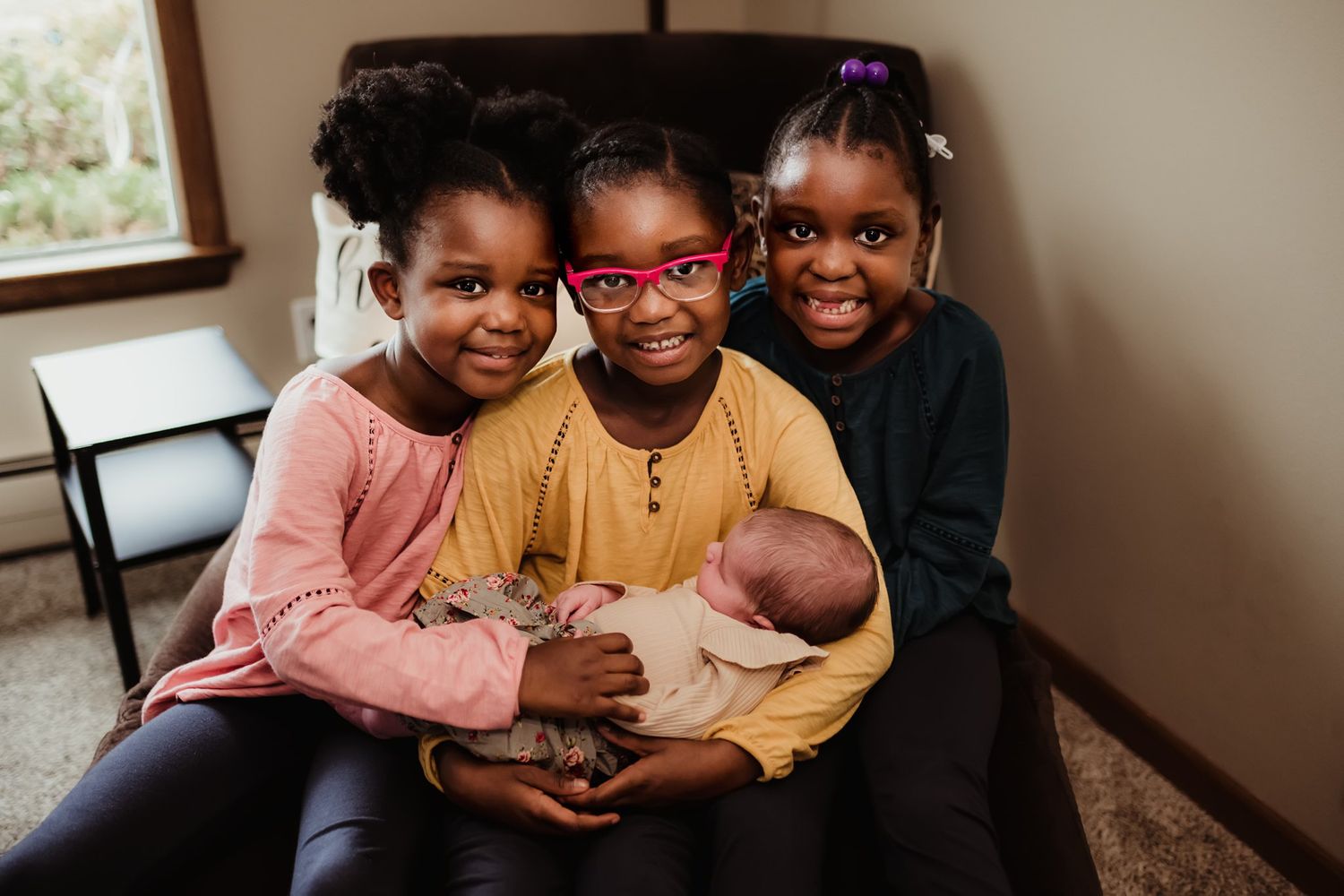 Three siblings sitting together on couch while carefully holding newborn baby.