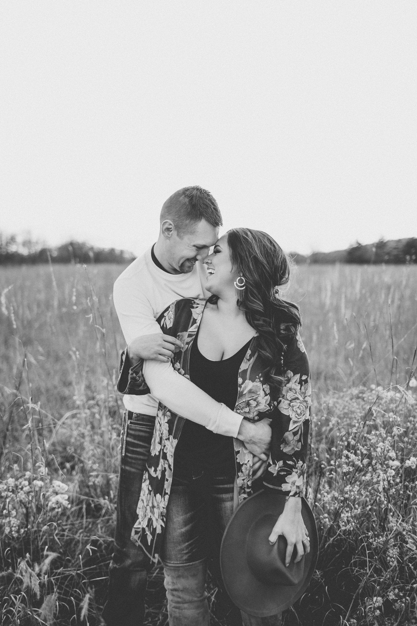 A black and white portrait captures an intimate moment between a couple in a wildflower field.