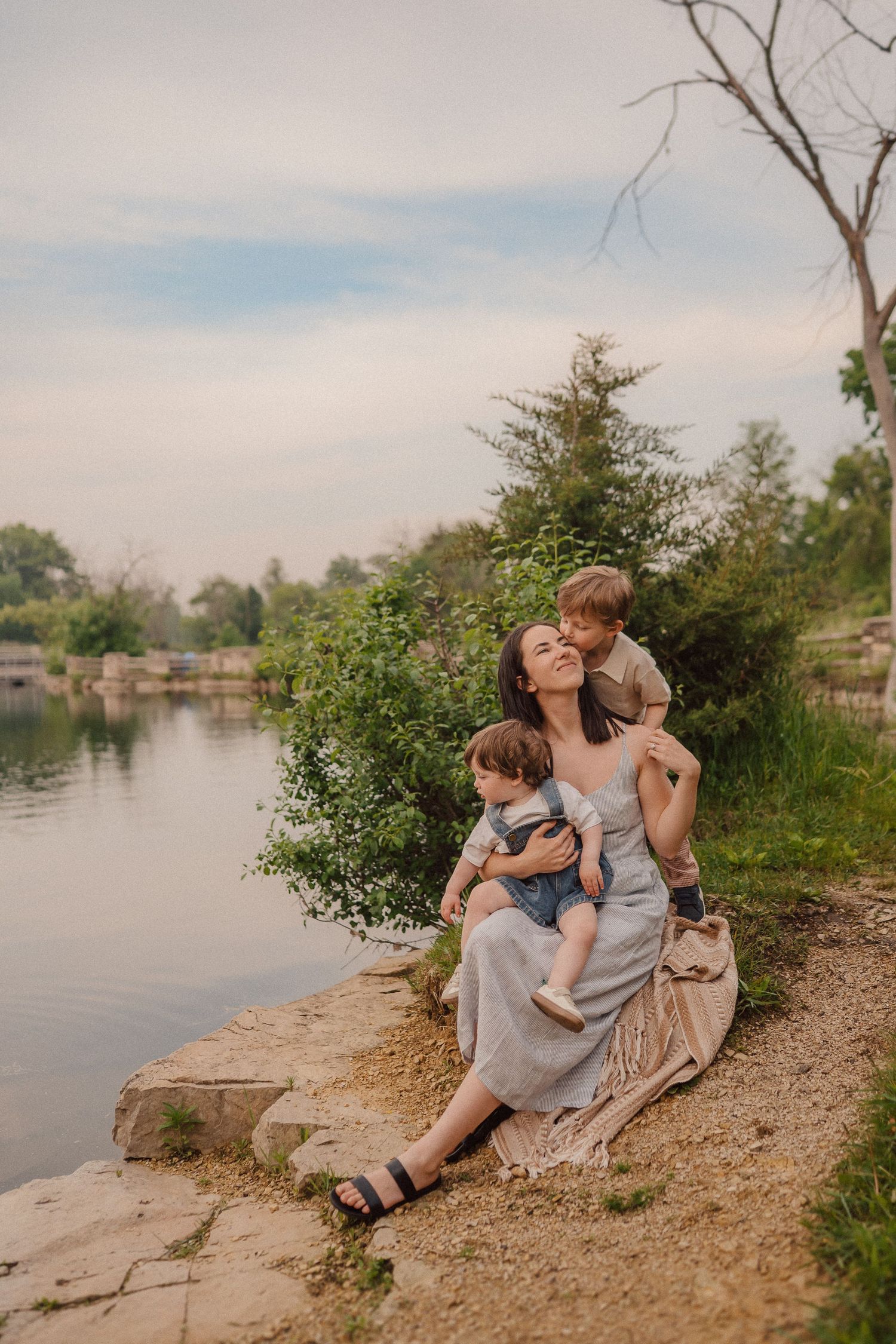 A family relaxes together on a rocky riverbank during sunset, enjoying a peaceful outdoor moment.