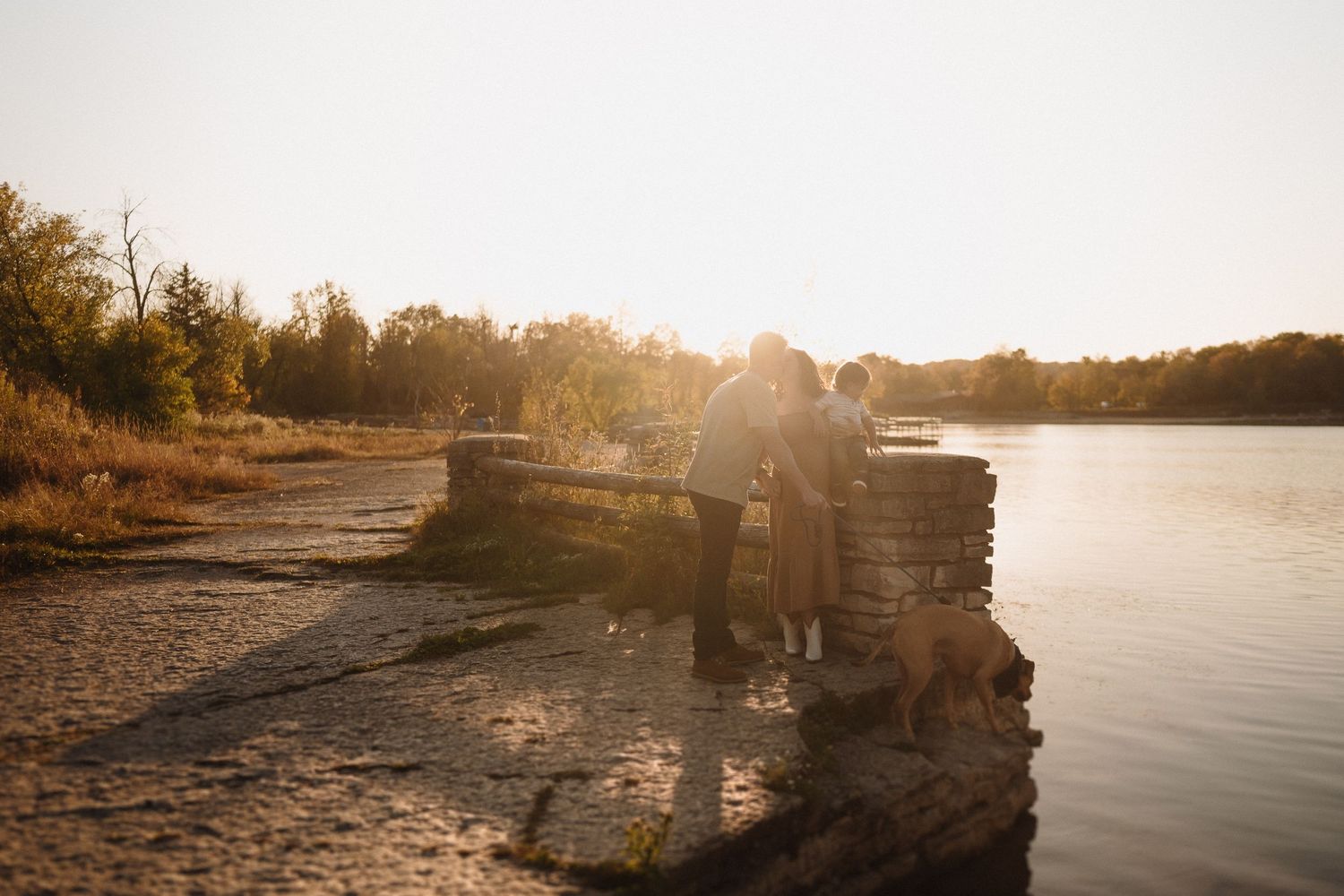 Romantic silhouette of a couple standing on a rocky ledge by a lake at sunset.