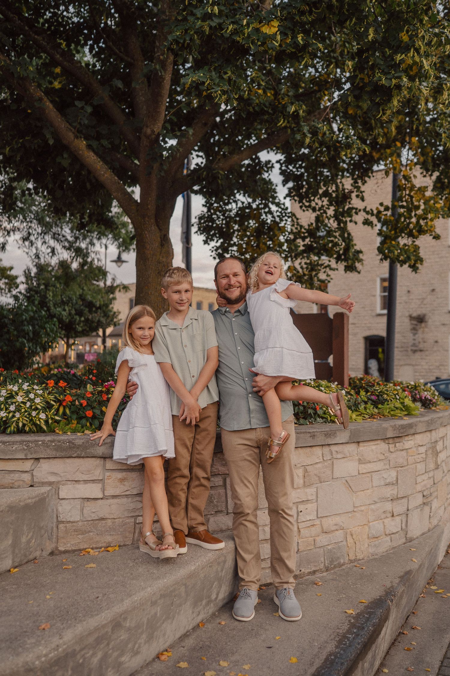 A casual outdoor photo session by a stone wall under trees.