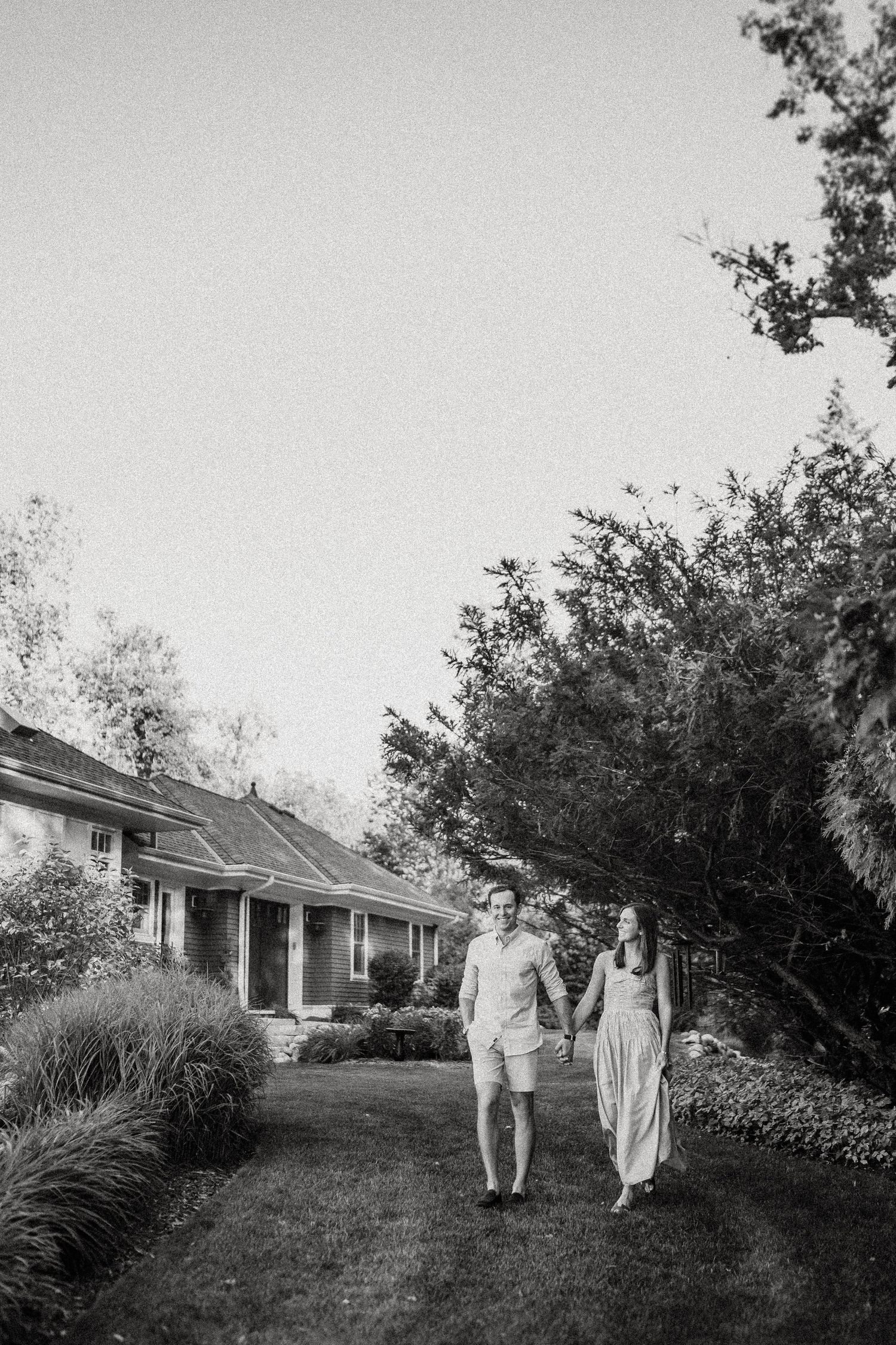 Black and white image of two people walking on a lawn in front of a house.