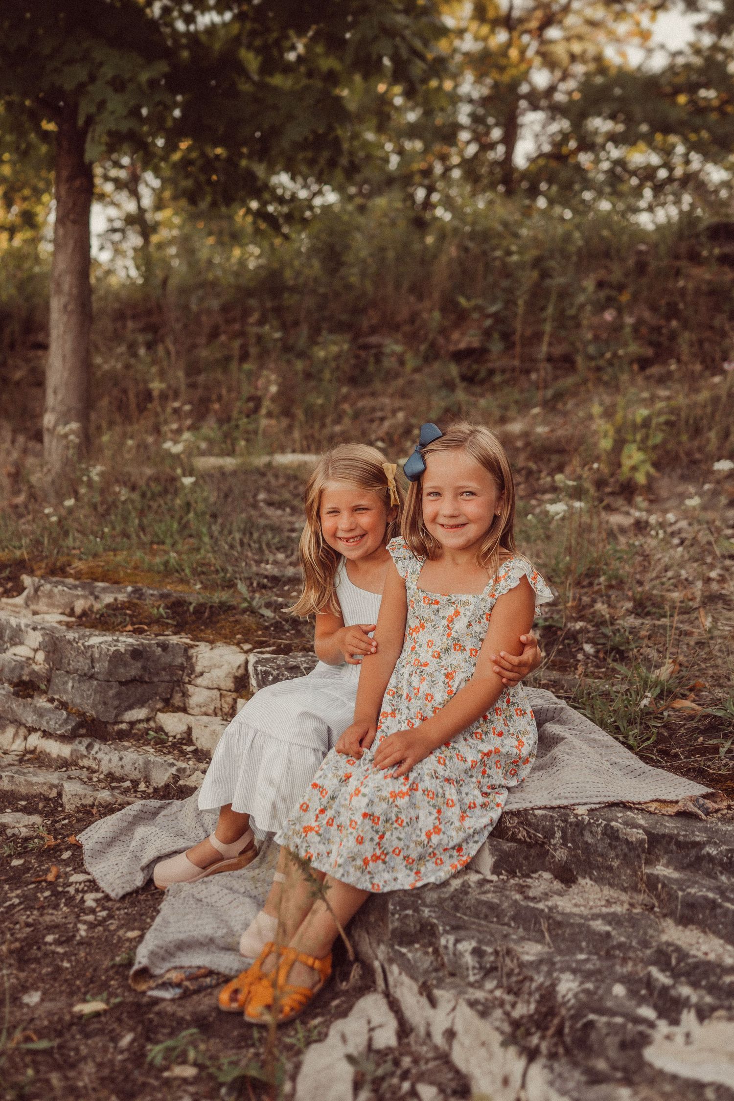 Two young children sit together on a rocky outcrop in matching summer dresses.