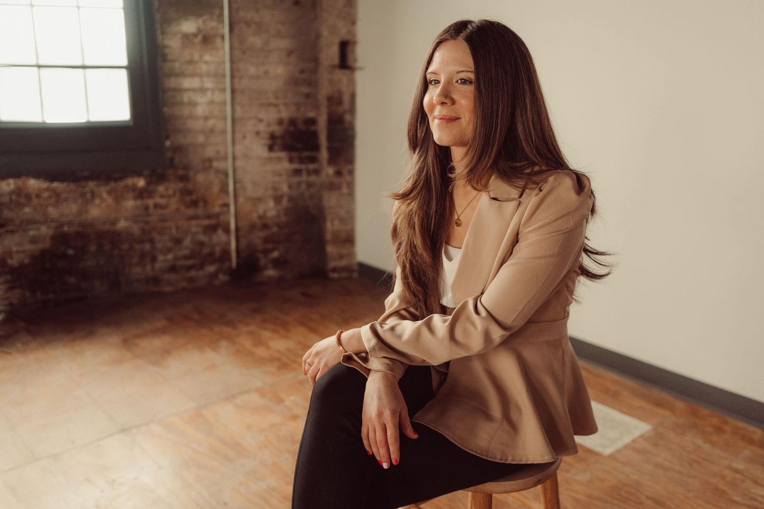 Natural light portrait in casual business wear against exposed brick wall background.