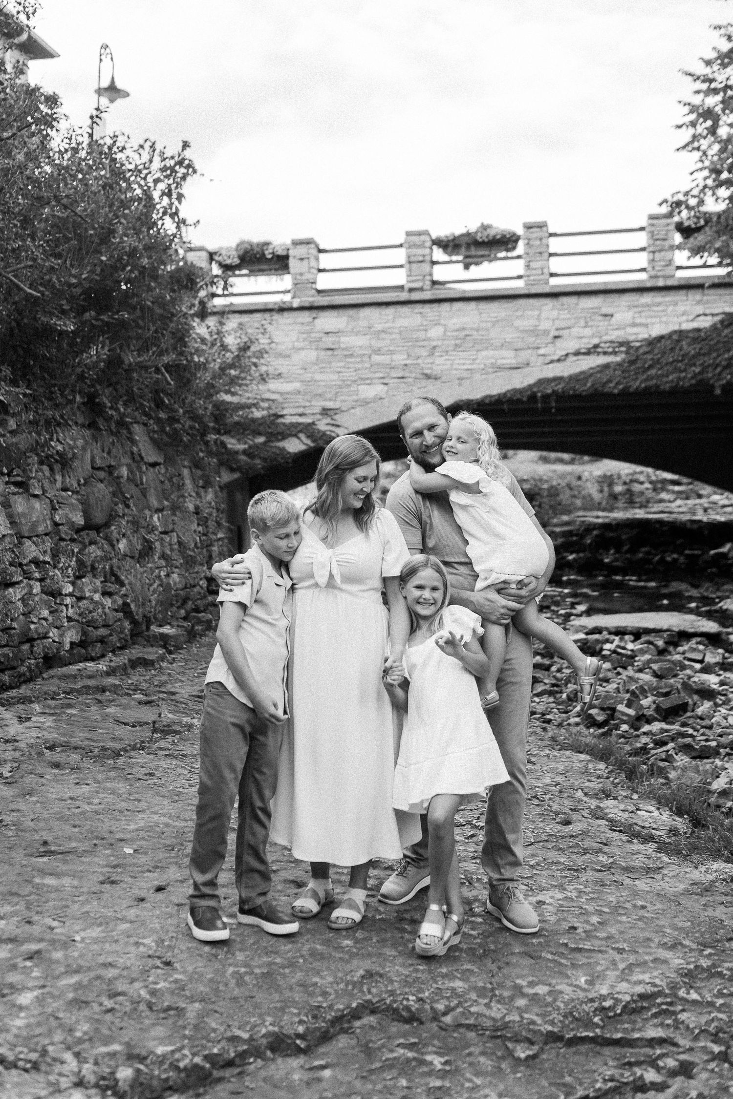 Black and white portrait of a family gathered near a stone bridge over a rocky creek bed.