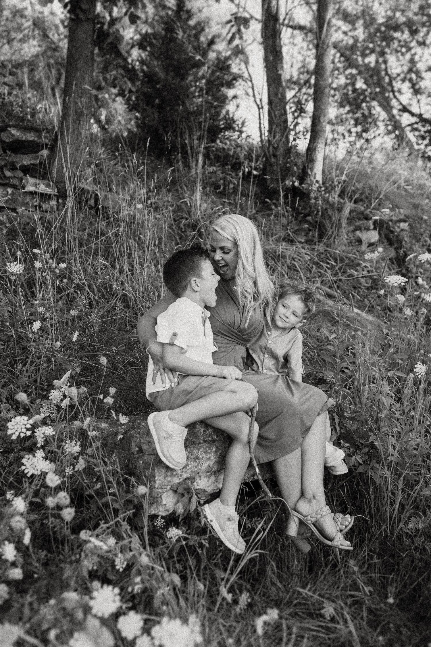 A black and white portrait of a family sitting together in a natural woodland setting.