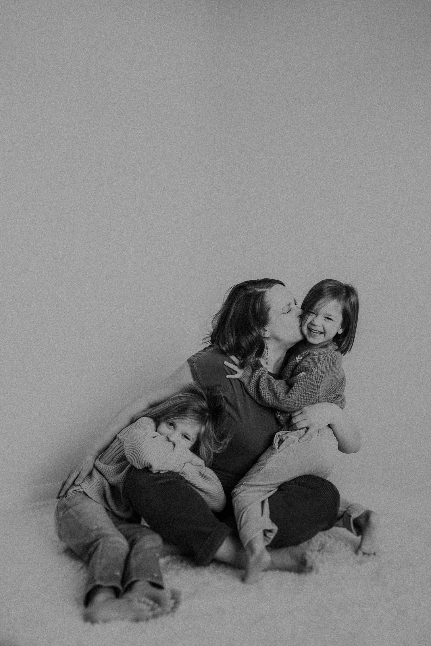 Candid black and white photograph capturing playful family moments on light background.