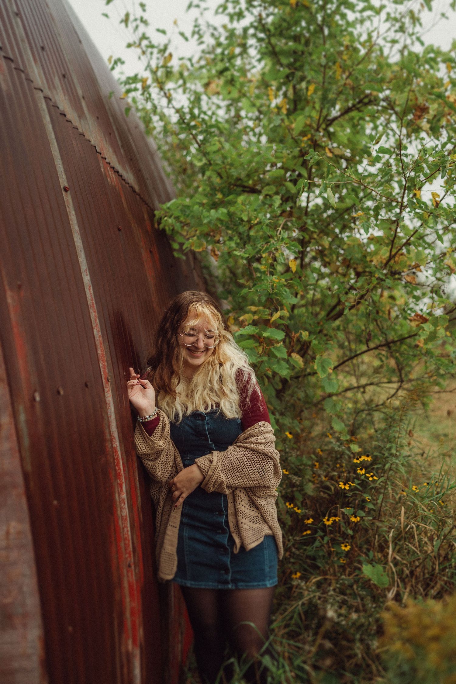 Candid outdoor portrait against rustic red metal structure surrounded by autumn foliage.