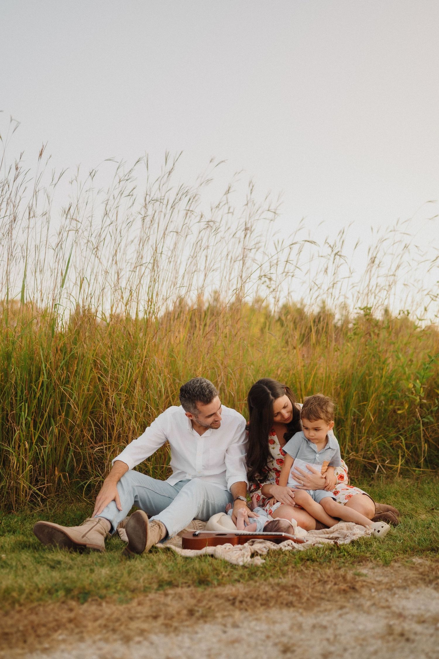 Family having a picnic on a blanket near tall grass during golden hour.
