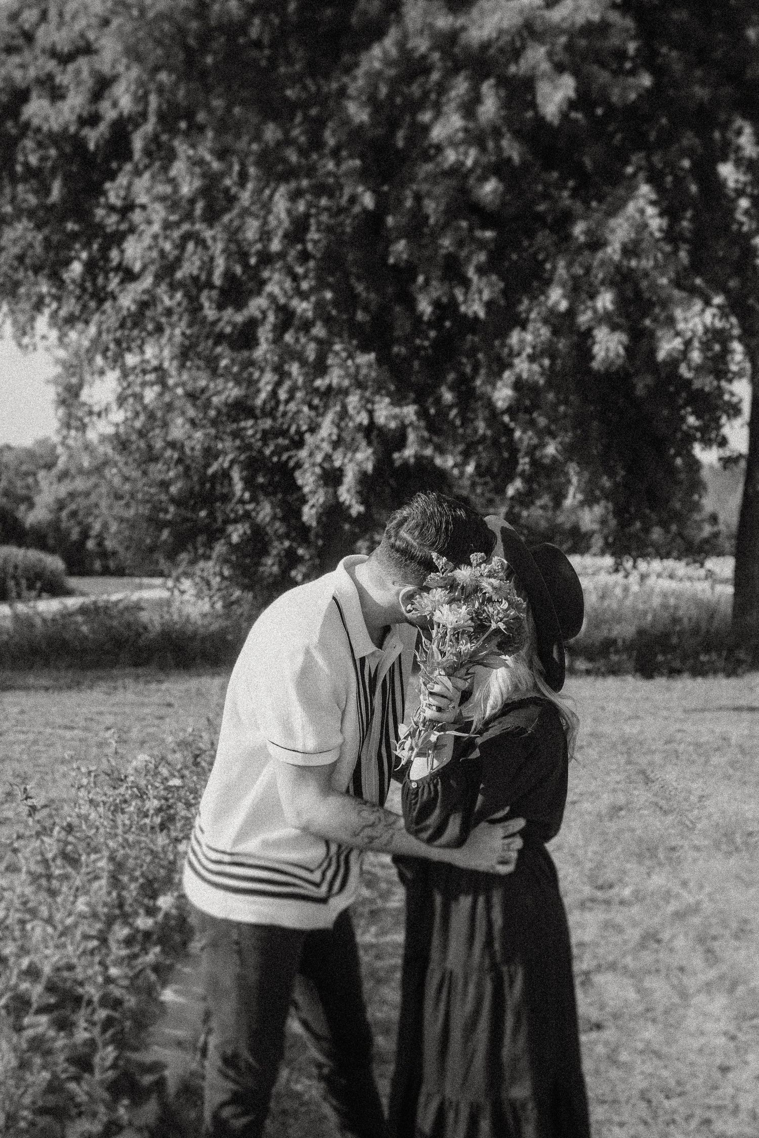Romantic black and white photograph of a couple embracing in a garden setting.