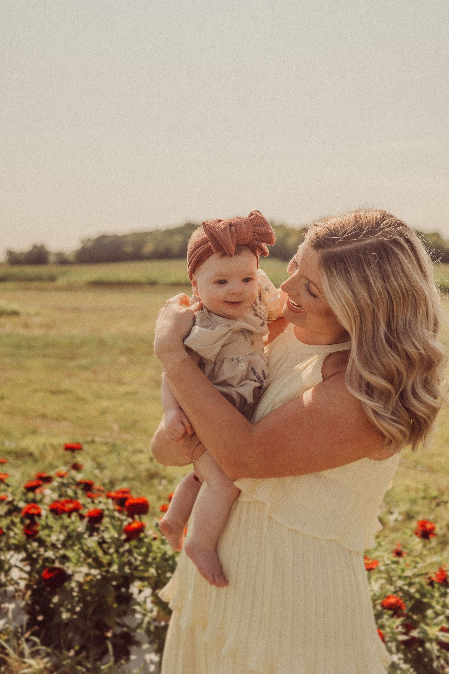 Sweet moment captured between mother and baby against backdrop of red flowers.