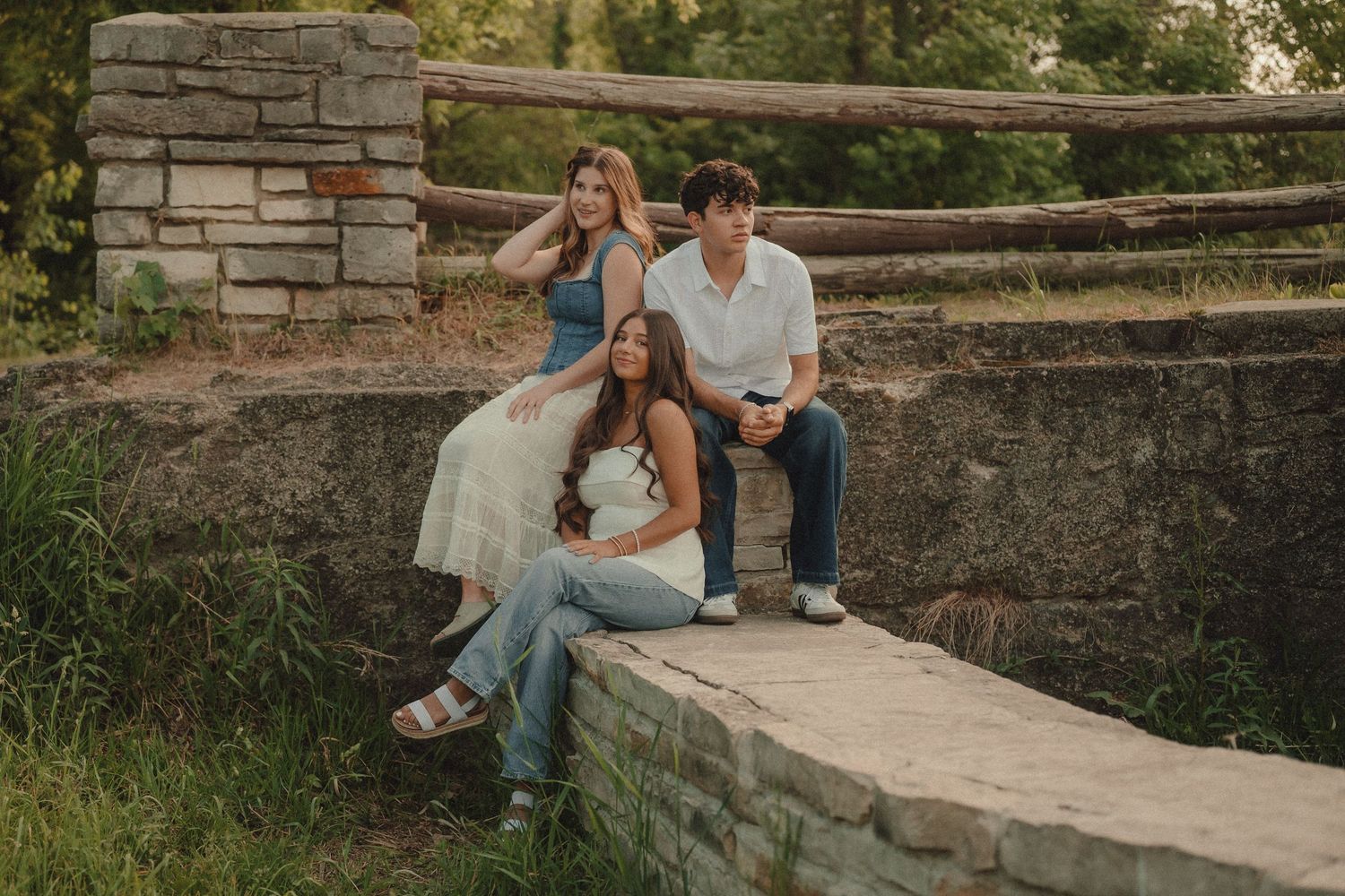 Three young adults pose on a stone bridge surrounded by lush greenery in a casual outdoor photo session.