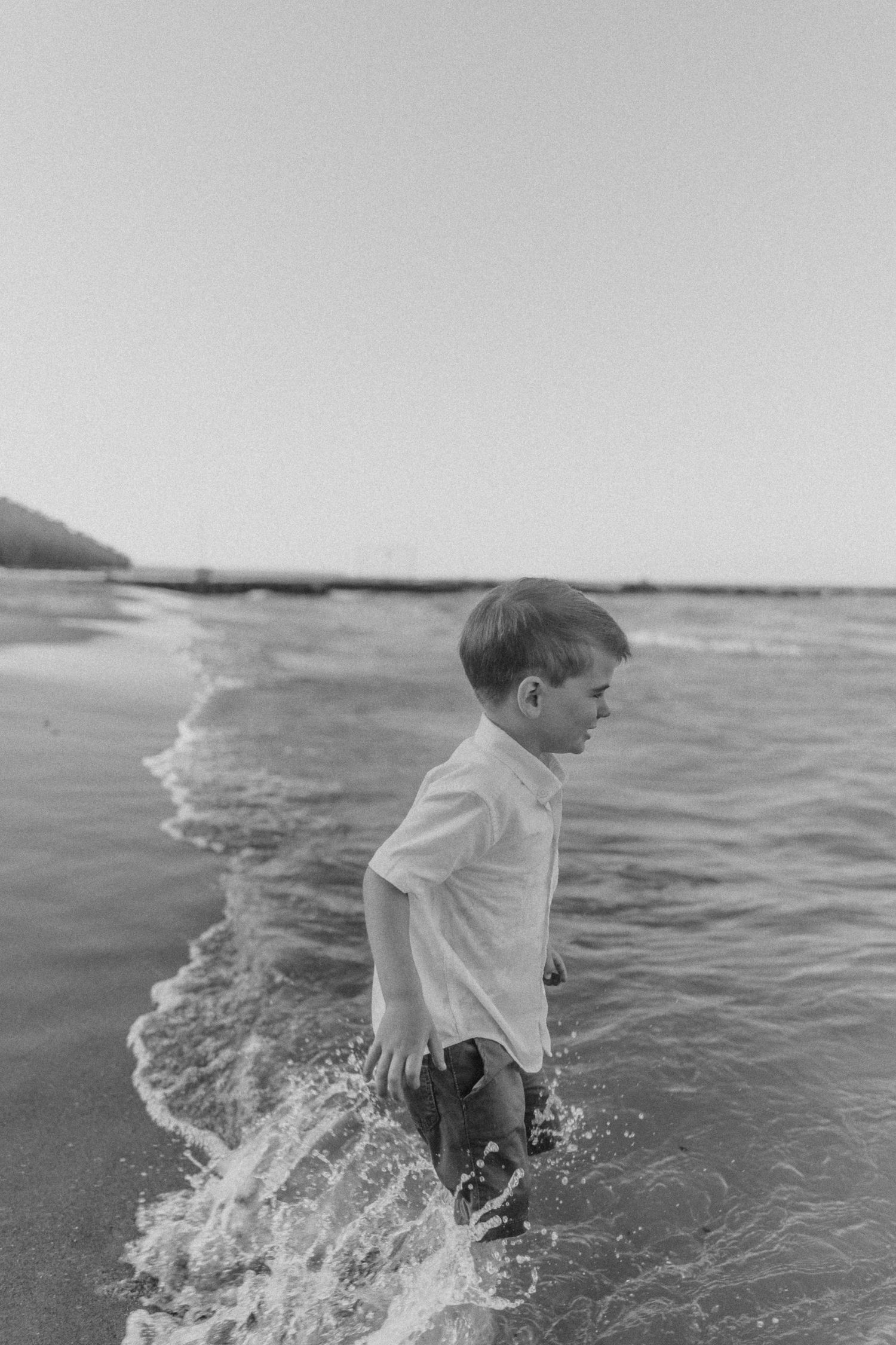 A young child in a white shirt splashes in the ocean waves along the shoreline.