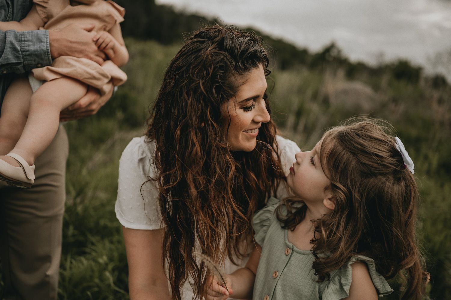 A tender outdoor family moment captured in soft natural lighting amidst tall wildgrass.