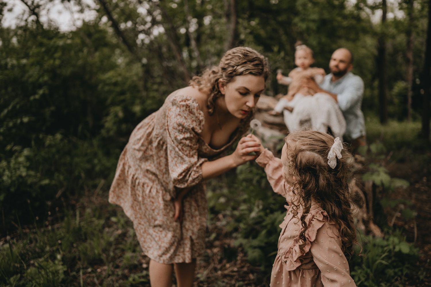 A tender moment shared between family members wearing matching dusty pink dresses in a woodland setting.