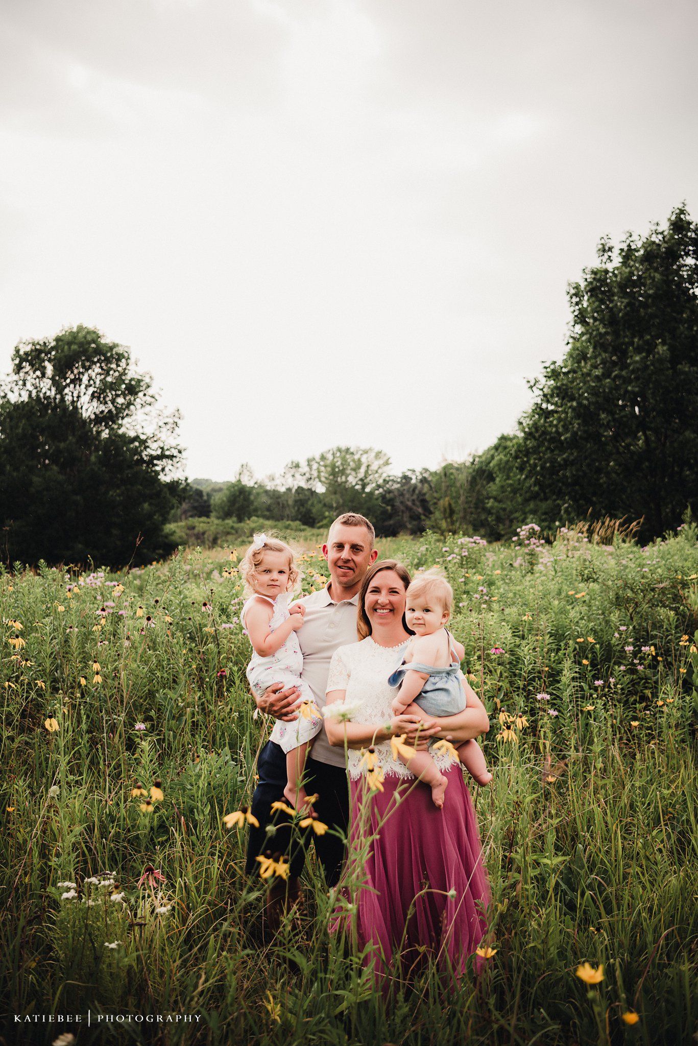 Family of four poses together in a meadow filled with yellow wildflowers.