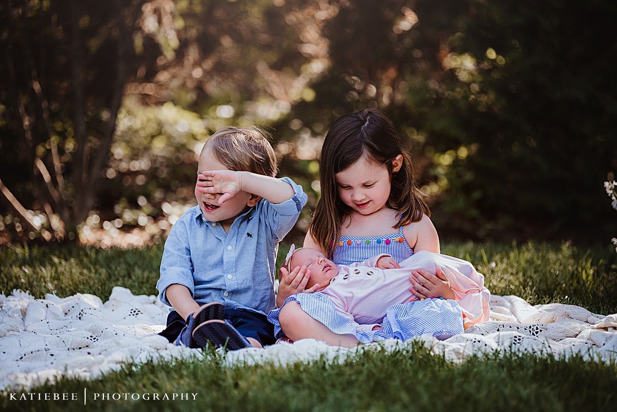 Children sharing a playful moment together on white blanket during outdoor photoshoot.