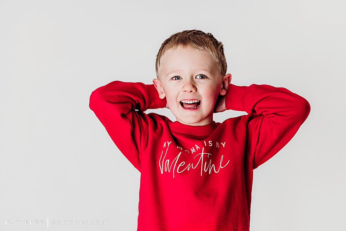 Playful child in red Valentine's sweater making silly expression on white background.