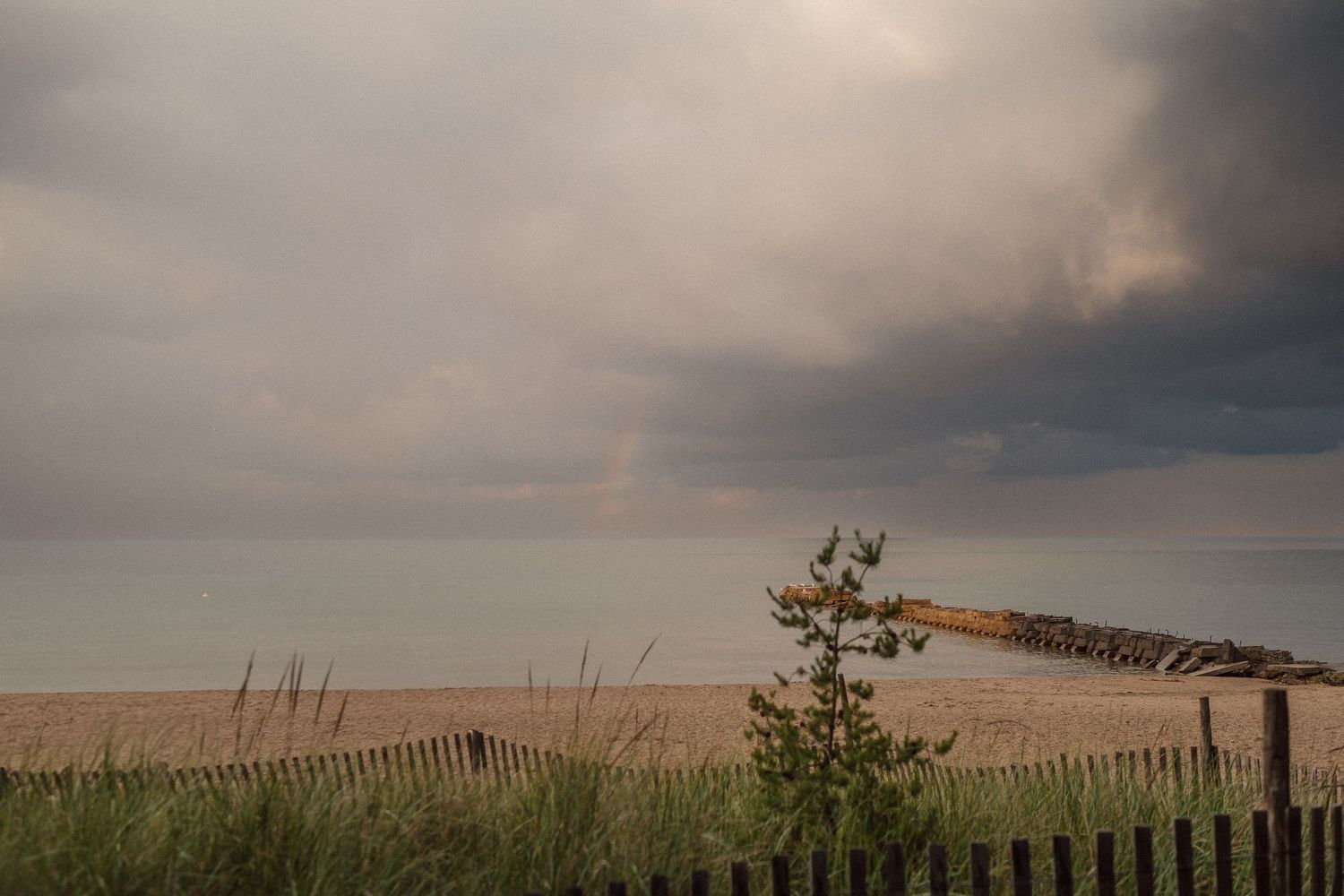 Moody coastal landscape with wooden fence along beach dunes under dramatic cloudy skies.