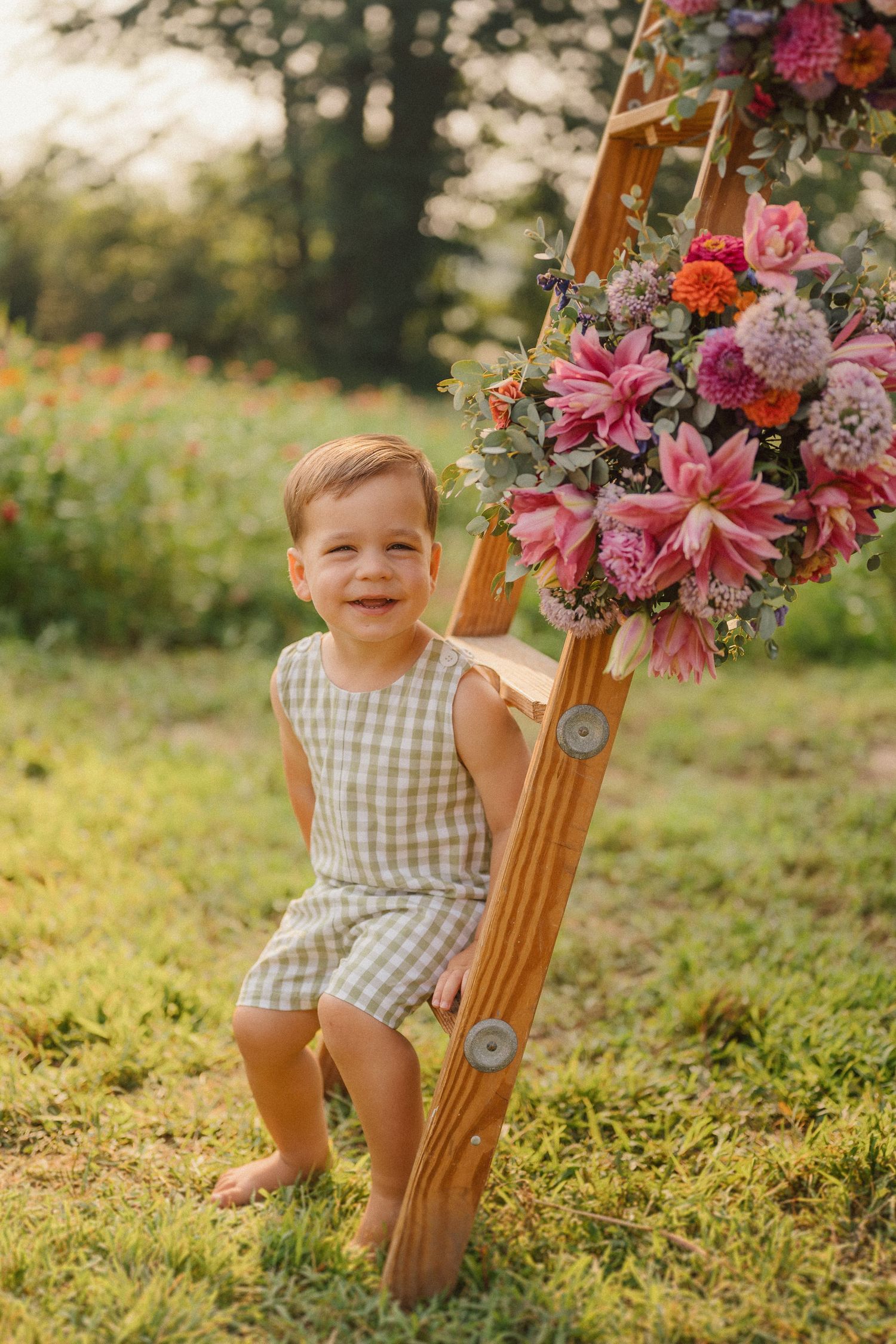 Baby sitting by wooden stand decorated with pink flowers in outdoor garden setting.
