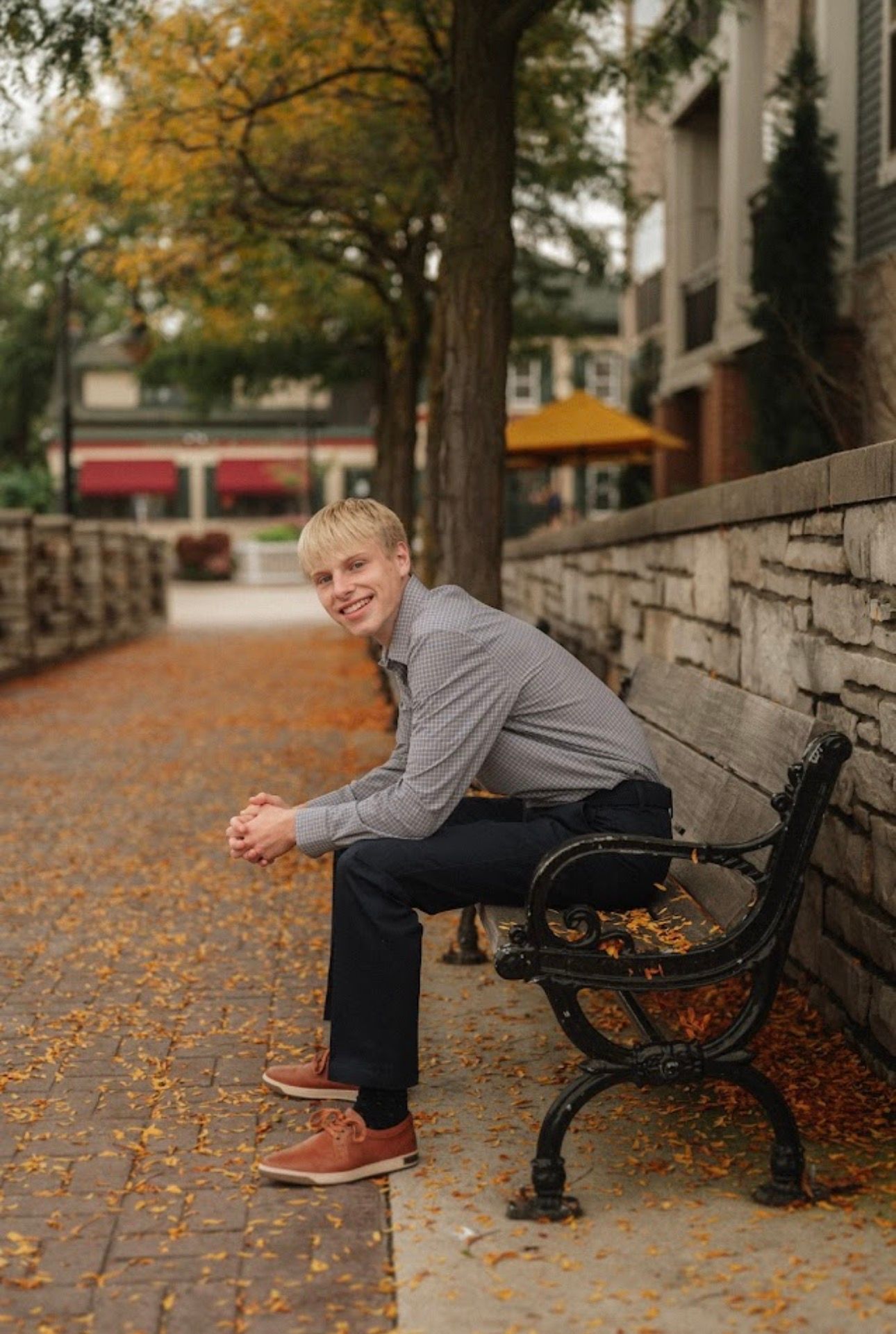 Autumn portrait session on a brick wall covered with fallen orange leaves.
