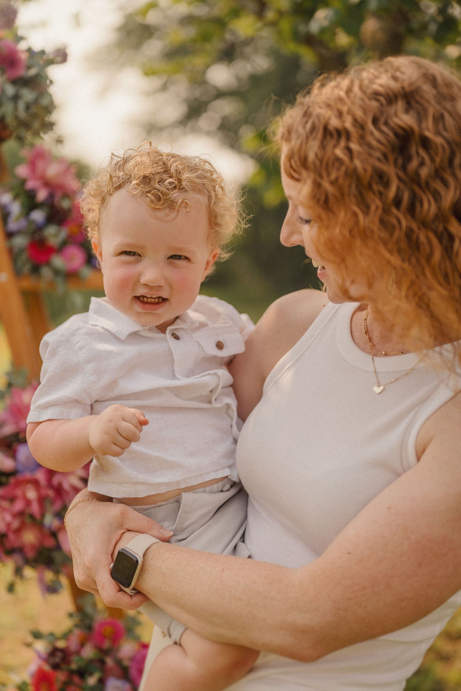 Tender interaction between parent and child outdoors against a backdrop of pink flowers and natural light.