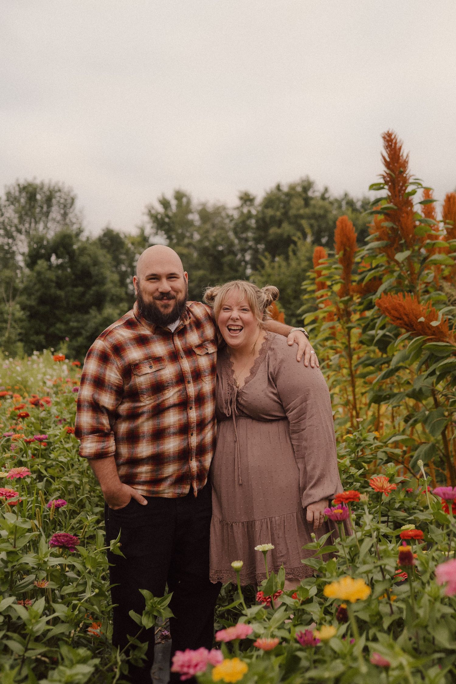 Two people share a joyful moment while embracing in a vibrant flower garden with autumn foliage.