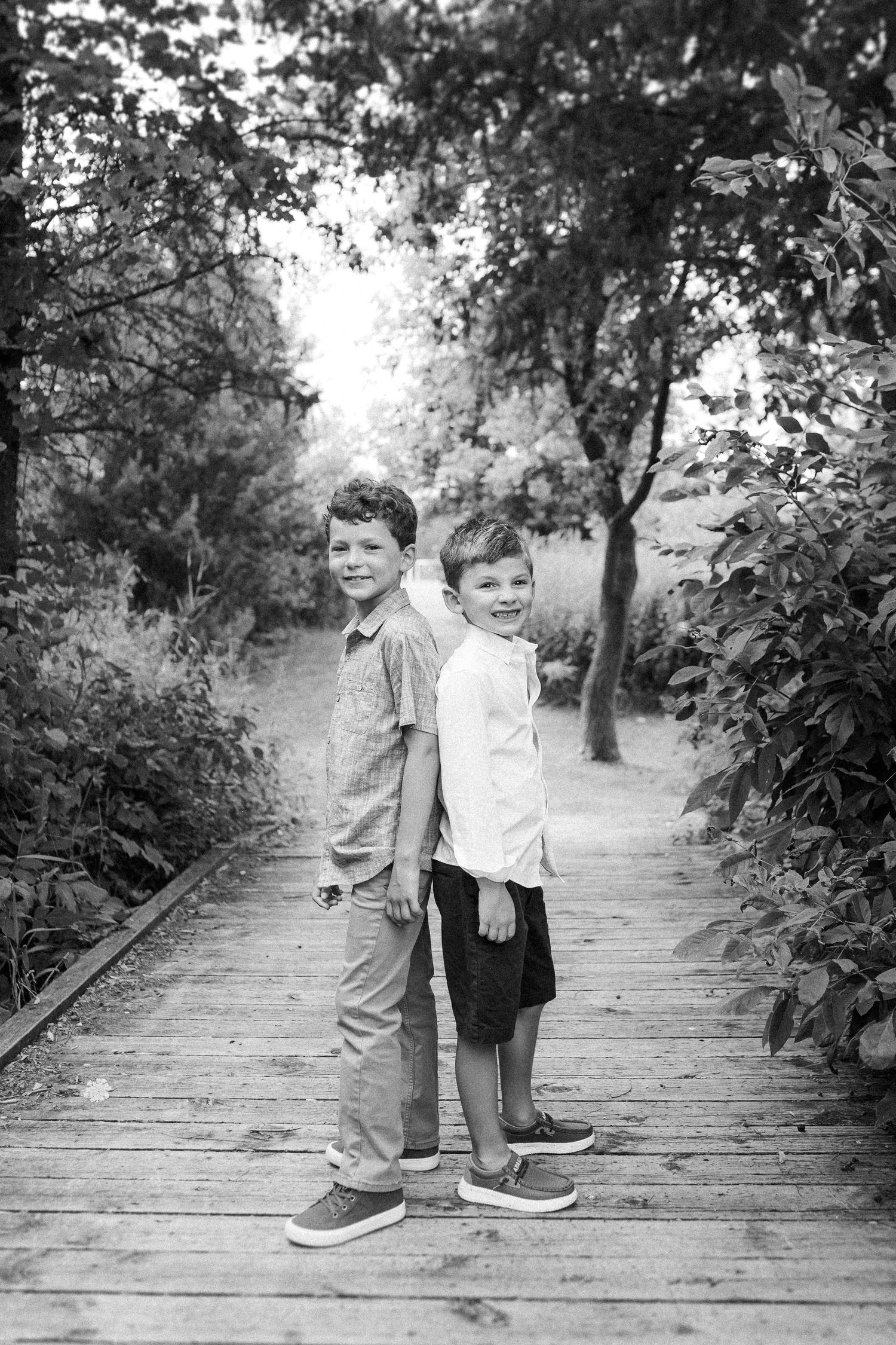 Children play and laugh together on a rustic wooden pathway lined with green foliage.