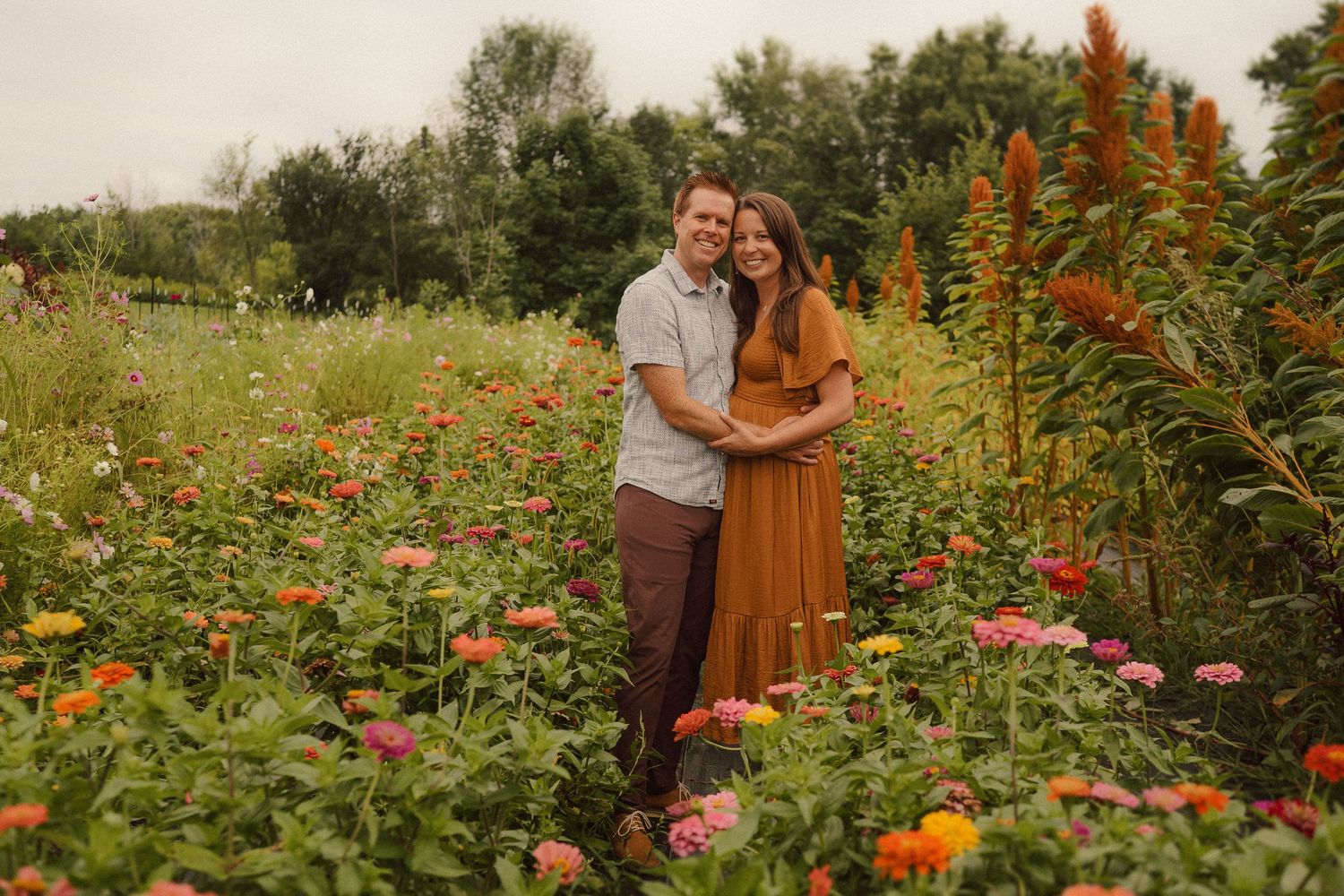 A couple embraces in a colorful wildflower garden with tall orange flowers and pink zinnias at sunset.
