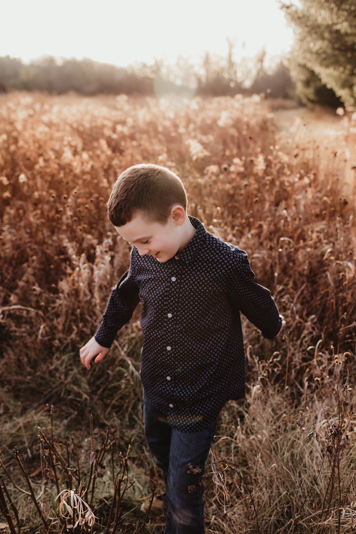 Child in dotted shirt walking through tall grass during golden hour.
