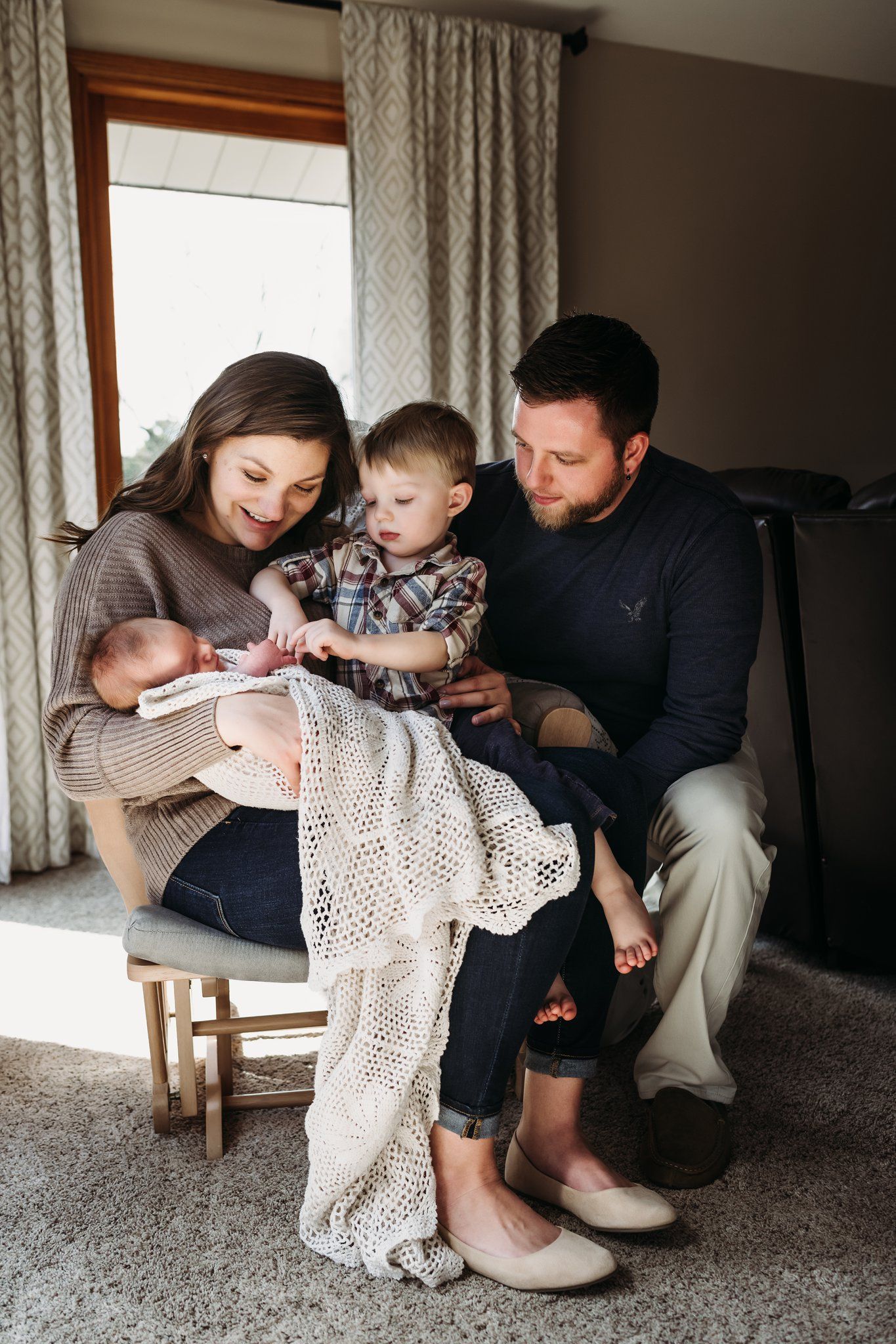 Family gathered in rocking chair sharing special moment together near window.