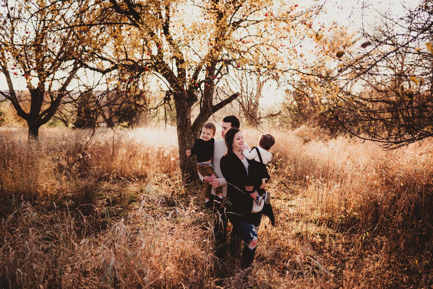 Family portrait in a serene field with autumn trees at golden hour.
