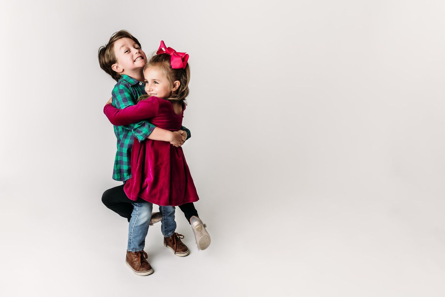 Two children in green shirt and red dress dance together on white background.