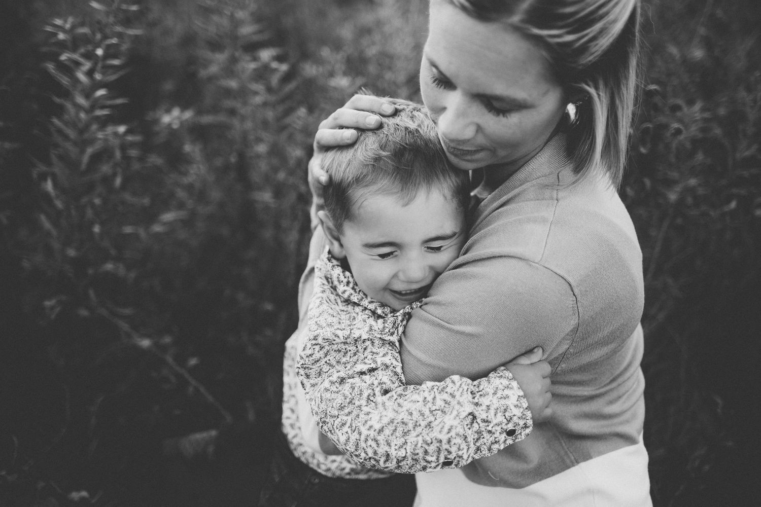 Black and white portrait of parent and child sharing a tender embrace outdoors.